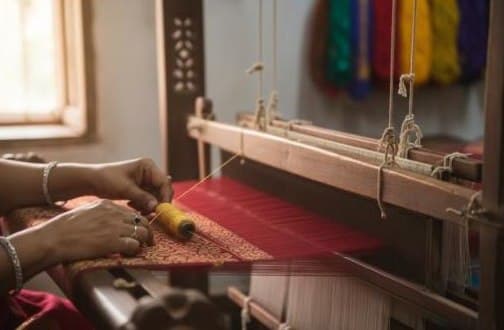 Hands weaving zari on a traditional loom